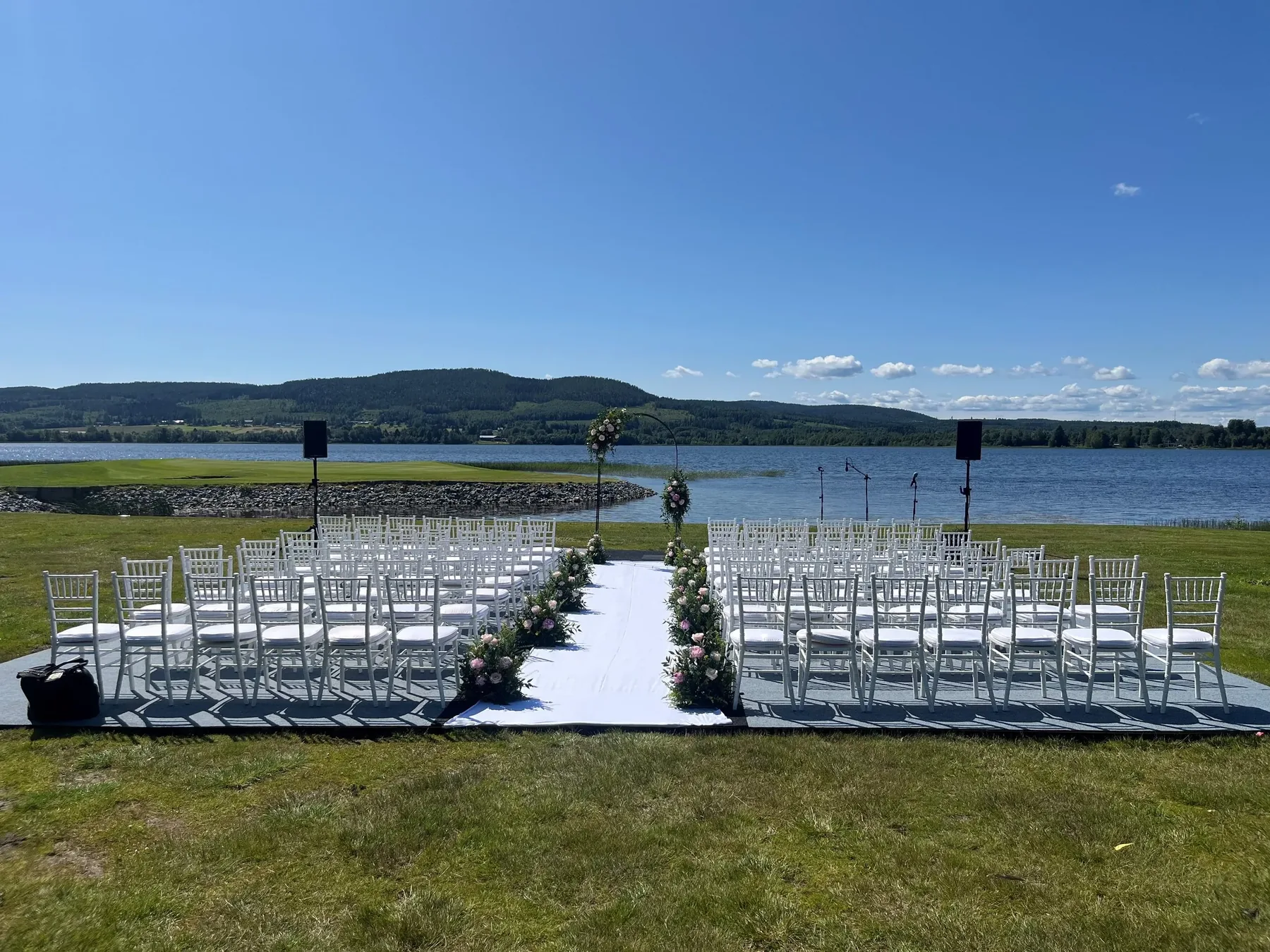 Utomhusbröllop med vita stolar och ljudanläggning vid vattnet utanför Örnsköldsvik